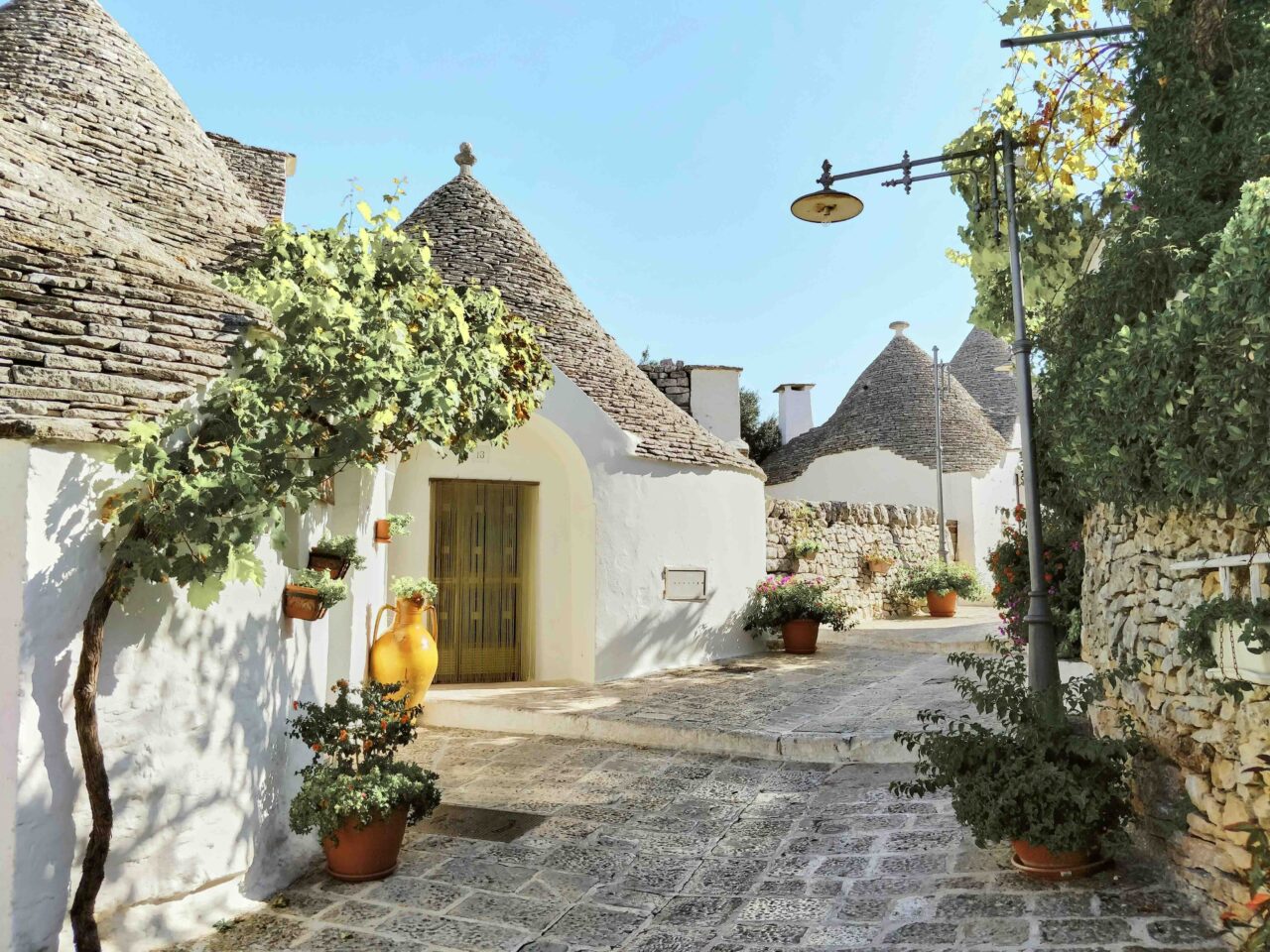 Photo village des Pouilles maison blanche et toits typiques ruelle pavée pots de fleurs