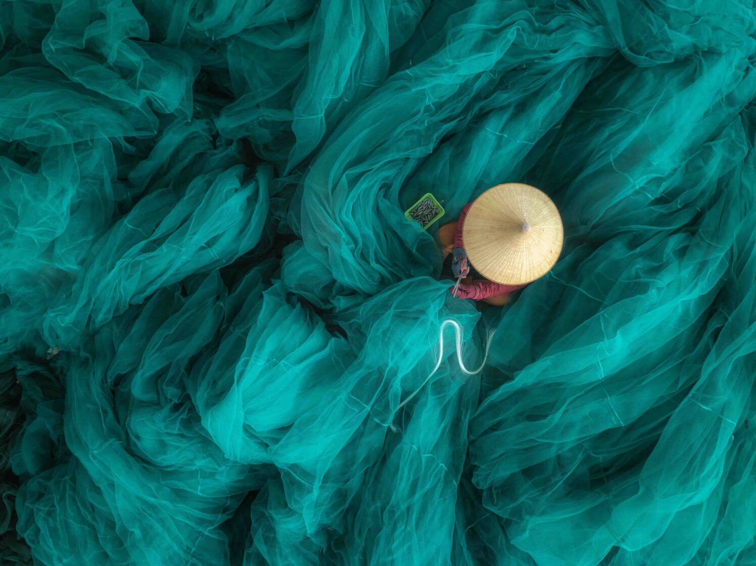 vue en plongée d'une femme en train de réparer un filet sur un grand et magnifique filet de pêche turquoise, au quai de Hon Ro, dans la ville de Nha Trang, province de Khanh Hoa, au centre du Vietnam.
