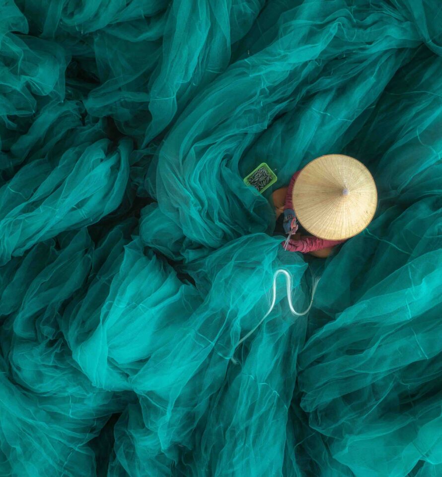 vue en plongée d'une femme en train de réparer un filet sur un grand et magnifique filet de pêche turquoise, au quai de Hon Ro, dans la ville de Nha Trang, province de Khanh Hoa, au centre du Vietnam.