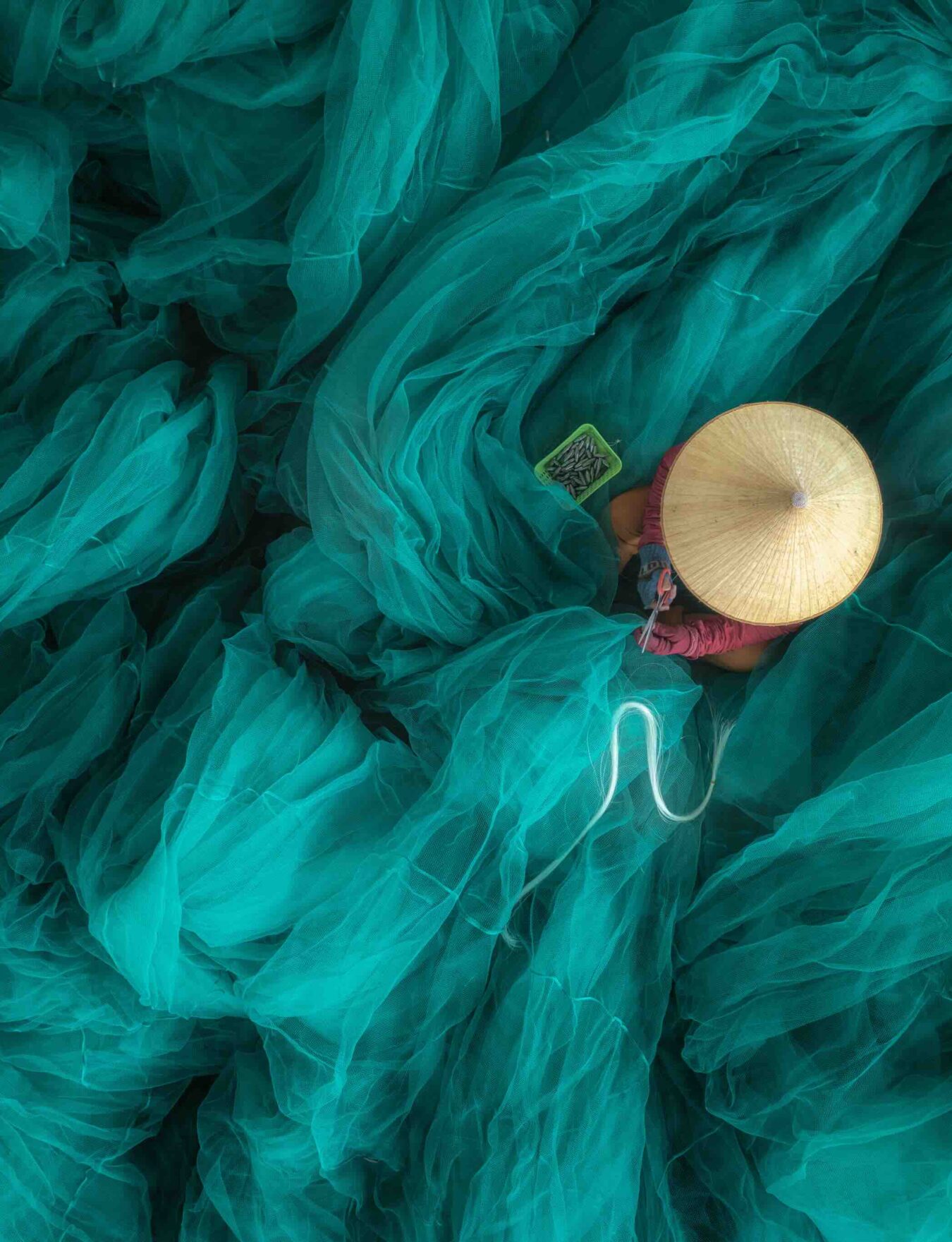 vue en plongée d'une femme en train de réparer un filet sur un grand et magnifique filet de pêche turquoise, au quai de Hon Ro, dans la ville de Nha Trang, province de Khanh Hoa, au centre du Vietnam.
