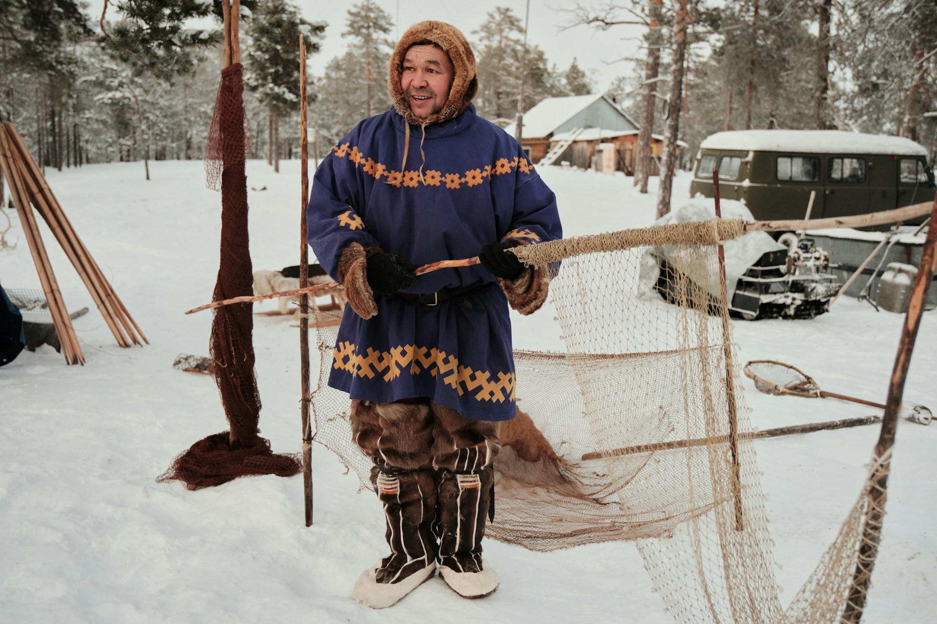 Homme en tenue traditionnelle présentant un filet dans un paysage enneigé de Laponie.