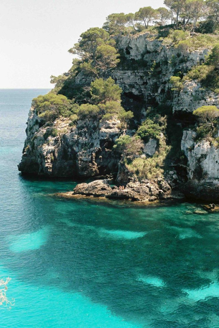 Crique sauvage aux eaux turquoise bordée de falaises et de pins à Minorque.