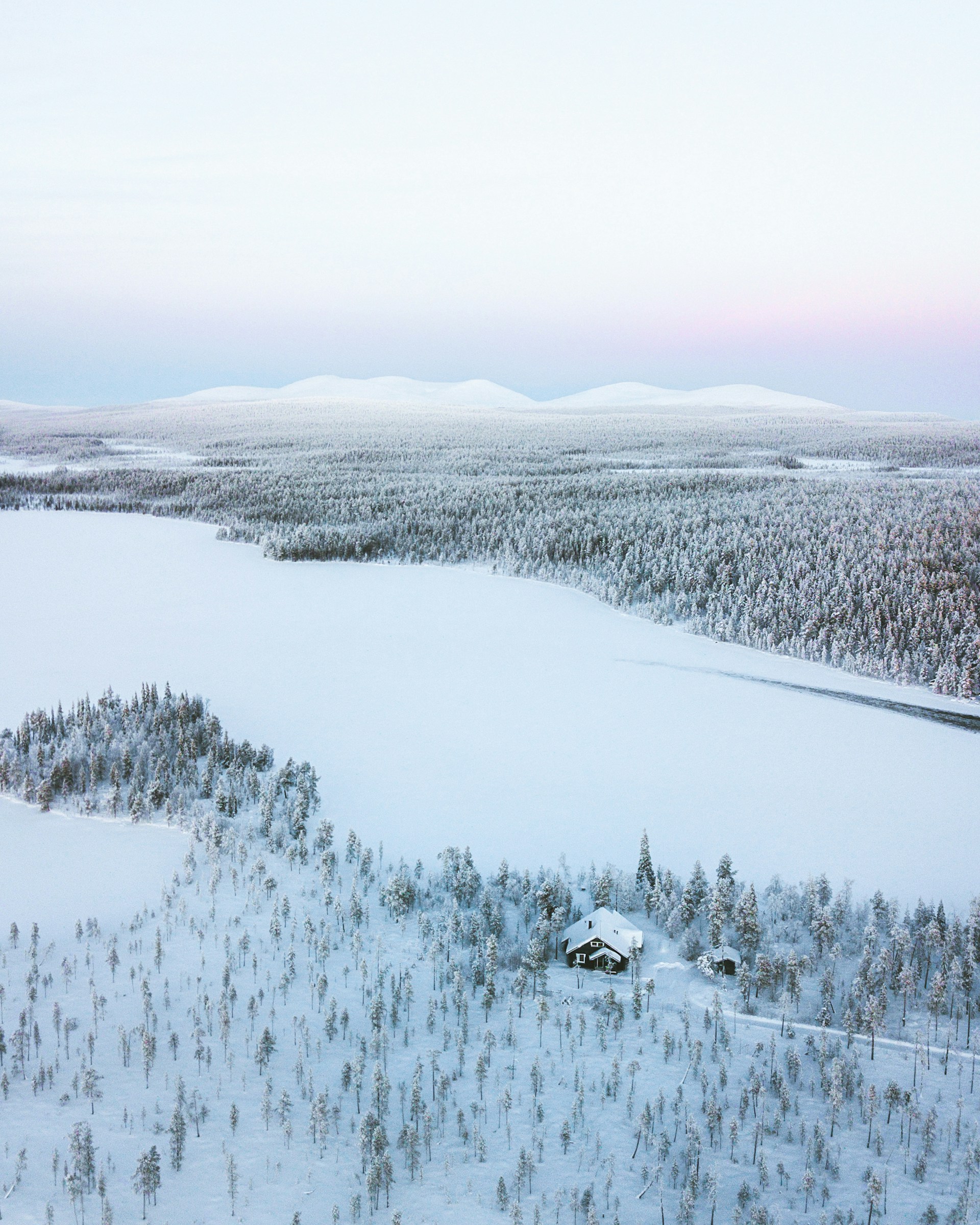 Vue aérienne d’un lac gelé entouré de forêts enneigées et de collines en Laponie finlandaise.