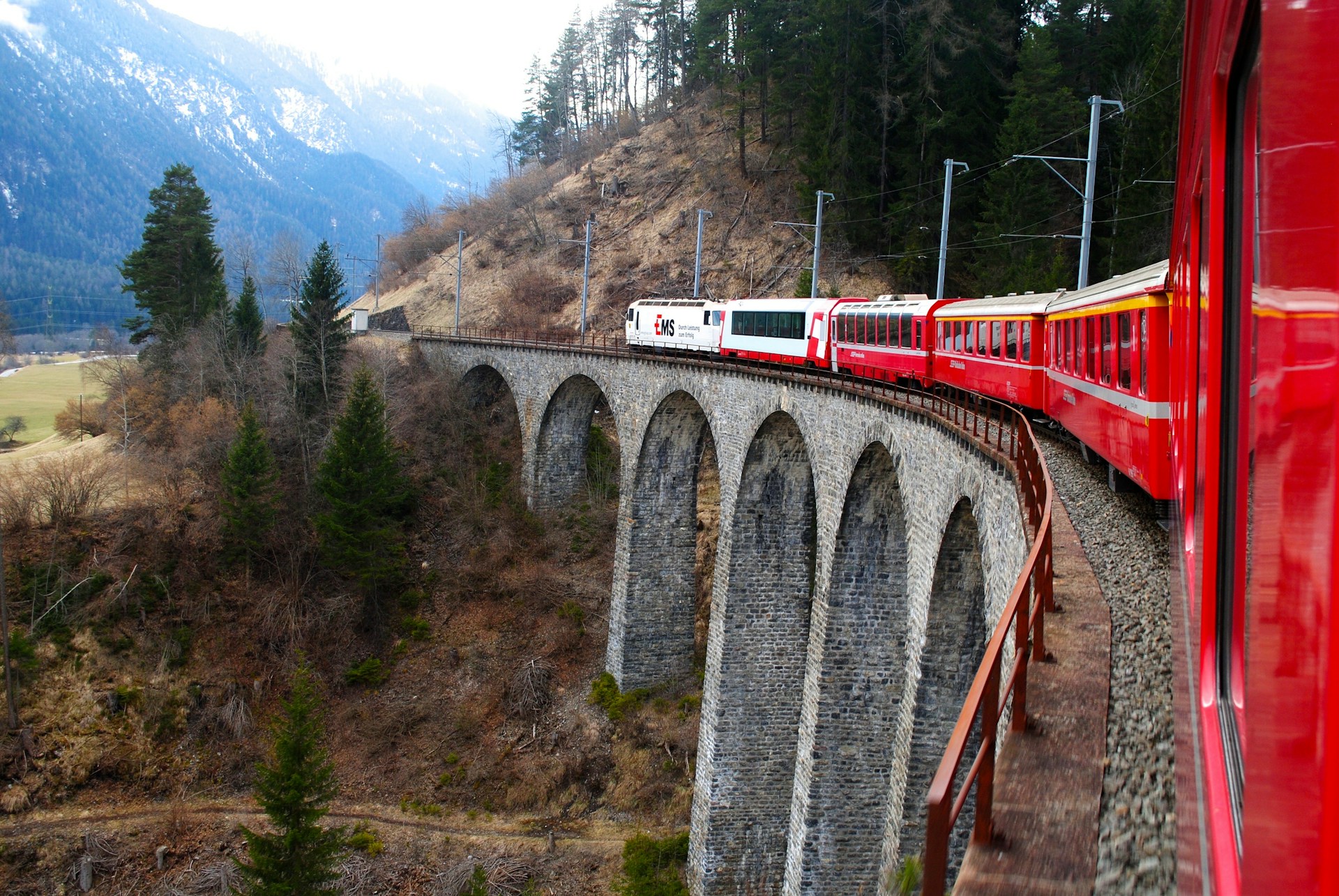 Train panoramique rouge traversant un viaduc de pierre dans les Alpes suisses